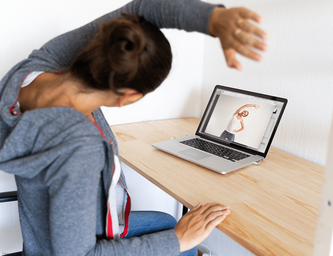 cs-pleaz-internal-1 a woman follows along with a video as she stretches while seated at a desk